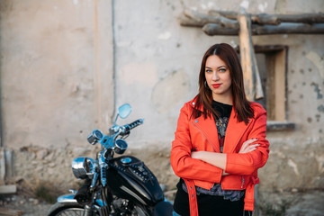 Fototapeta na wymiar beautiful young blue eyed woman smiling in front of her motorbike, wearing a jacket and red lips