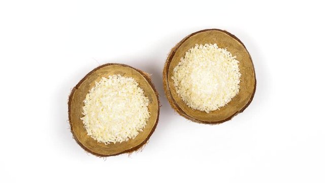 Top view of two shells halves of tropical coconut with dried white coconut flakes rotating on white isolated background. Healthy tropical fruits. Loopable seamless cocos rotating