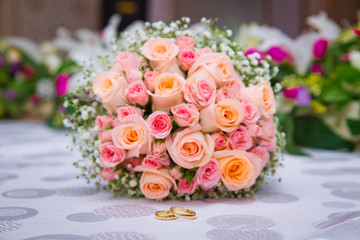 Bridal bouquet with orange and pink roses of different size with handle on white background. Wedding bouquet with beautiful flowers. Two rings represent the meaning of feeling love. Selective focus