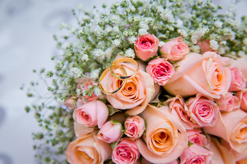 Bridal bouquet with orange and pink roses of different size with handle on white background. Romantic wedding bouquet with beautiful flowers. Two rings represent the meaning of feeling love