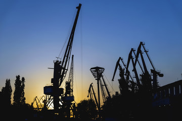 Fototapeta na wymiar Evening in port, sea, river dock. Silhouette of industrial cranes. Wharf, Port landscape. Bright sunset