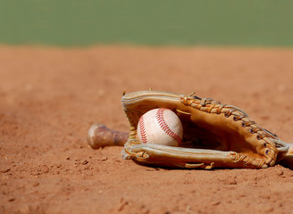 An old baseball glove cradling a worn ball lays in the dusty clay of the infield at a ball park on a sunny day. Shallow depth of field. Copy space. © Perry Correll