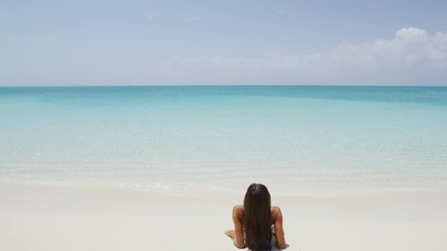 Beach travel vacation holidays. Woman enjoying sunbathing looking at ocean lying down in perfect white sand relaxing after swimming in amazing turquoise water. Serene nature. RED EPIC SLOW MOTION