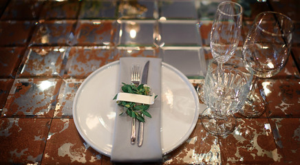Mirror table served with plates, forks, spoons, glasses,  napkins in the restaurant. Beautiful festive table