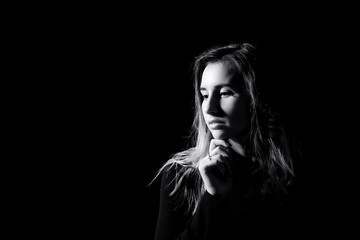 girl in black holds her hand under her chin and looks down thoughtfully with a place for writing on a black background close-up black and white image