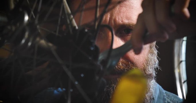 Well-groomed handsome bearded master hipster, specialist in bicycles, repairing a bicycle in his workshop, wheels, frame, spokes, the background of tools. Concept: pro bike, cycle passion, lifestyle.