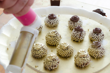 Process of sprinkling paint in chocolate granulated chocolate with crunchy balls and a chocolate flower on top. On a golden tray.