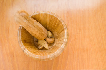 mortar with dried garlics about to be crushed in horizontal photo on wooden background