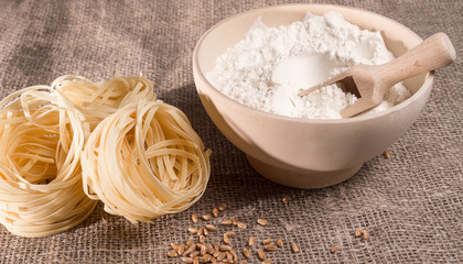 Macaroni, flour in a wooden cup on a background of burlap