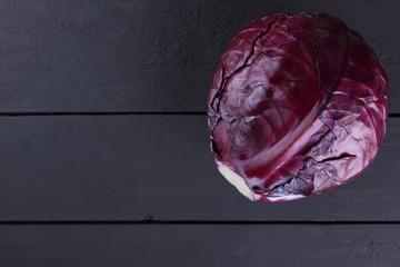 Purple cabbage on a dark wooden background, a whole cabbage on wooden planks of dark, purple vegetables, vegetarian food, copy space, a top view of vegetables in the style of minimalism
