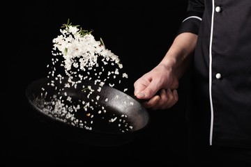Cooking roasted aromatic salt in a pan by chef hand. Horizontal photo view. Dark black background with copy text area