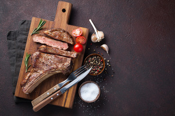 Fototapeta na wymiar Grilled cowboy beef steak, herbs and spices on a dark stone background. Top view with copy space for your text