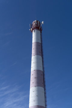 old brick factory chimney, used as a tower of cellular and distant radio communication, against the sky