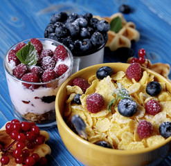 Healthy breakfast with corn flakes, berries, waffle and milk on blue background.