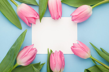 Birthday or wedding mockup with white paper list, pink tulip flowers on blue background top view. Beautiful woman day card. Flat lay