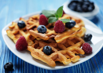 Traditional belgian waffles with fresh berrys and sugar powder on white plate, blue wooden background. Flat lay, top view, copy space.