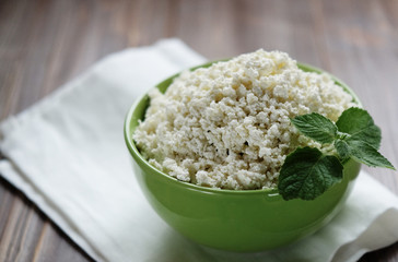 Cottage cheese with mint in a green bowl on a white napkin.