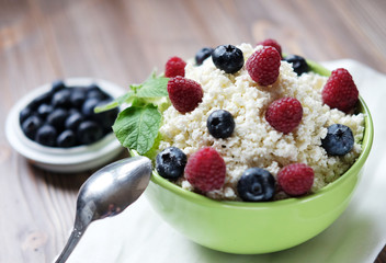 Cottage cheese in green bowl with raspberries and blueberries on wooden background. Healthy Breakfast.