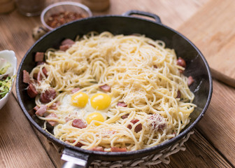 Spaghetti with sausages, cheese and quail eggs in a frying pan.