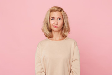 Obraz premium Indoor shot of doubtful pensive woman, curves her lip, feels uncertain, try to make choice. Isolated, over pink background