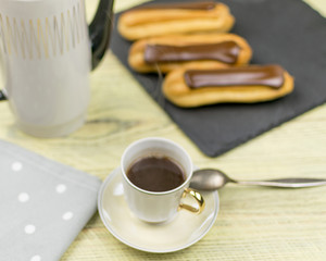 Eclairs and coffee on a wooden background.