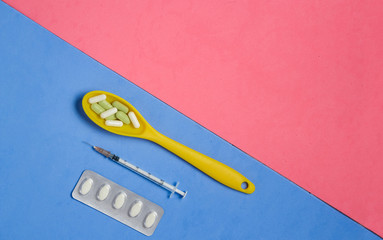 Pills and Capsules in Yellow Spoon, Syringe on Blue Background with Pink Copyspace.