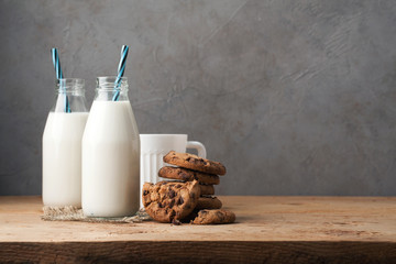 Two bottles of milk and chocolate chip cookies on dark background with copy space