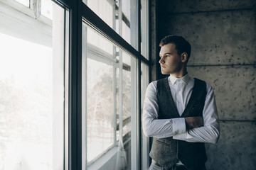 Young manager in suit standing in office with hands crossed on chest looking through the window.