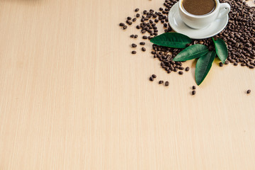 Cup of coffee on  coffee beans and leaf on the top left side wooden table with copy space