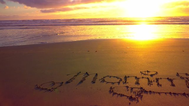 4k. Mother's Day Greeting Card. Mommy word on the sand. Sunset. Sandy Ocean Beach. Handwritten Inscription. Space for Text on Top. Golden, orange, yellow, pink, purple colors. Camera Moving to Right.
