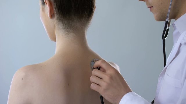Woman coughing hard, physician listening to her lungs, treatment of pneumonia