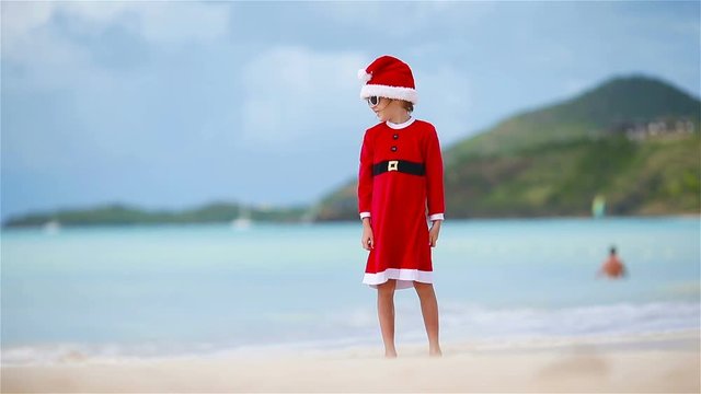 Adorable girl in Christmas hat on white beach during Xmas vacation