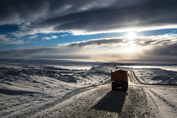 A truck running in the Arctic among the snows moves along the road toward the dawn.