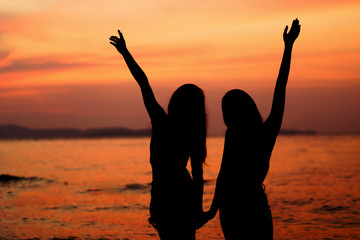 Fototapeta premium Silhouette of two woman having fun on the sea beach
