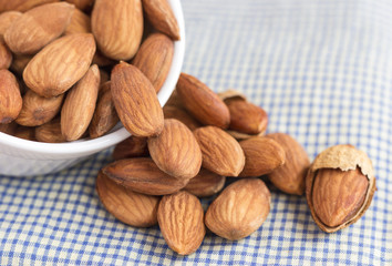 Almonds in a white ceramic bowl on the blue cloth background.