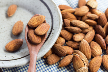 Almonds in the wooden spoon with a green ceramic dish on the blue cloth background.