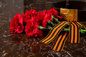 cloves, a military belt and a St. George ribbon on the background of the monument