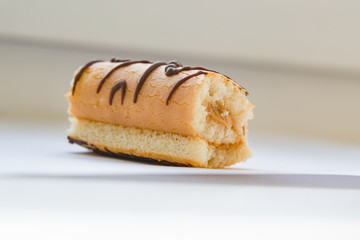 Piece biscuit cake mini roll with cream and chocolate pattern on light background, close-up 