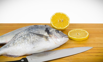 Dorado fish with lemon and knife on bamboo board, gilt-head bream