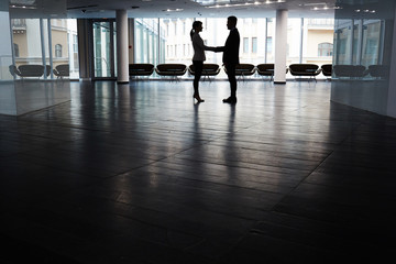 Unrecognizable entrepreneur shaking hand of male business partner after successful completion of negotiations, interior of dim spacious office lobby on background