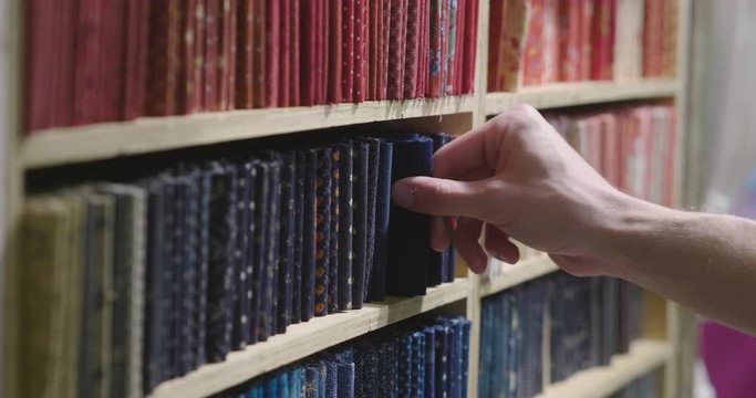 Close up of a man's hand taking a small book from a library full of colored books.