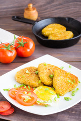 Crispy hash browns, chiken egg and tomatoes on a plate on a wooden table