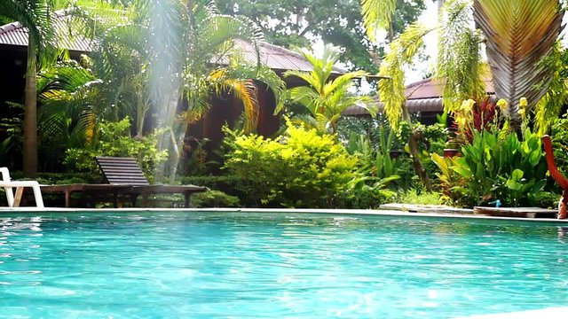 Swimming pool and palm trees in tropical garden with bamboo bungalow. paradise for tourists on sunny day with lens flare effects. slow motion. 1920x1080