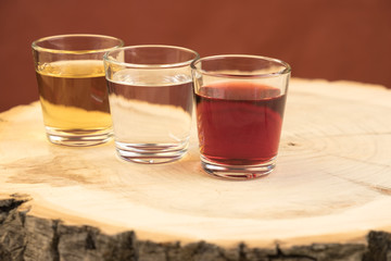 three glasses with different spirits are located on a wooden stump with annual rings, the texture of the cut is visible