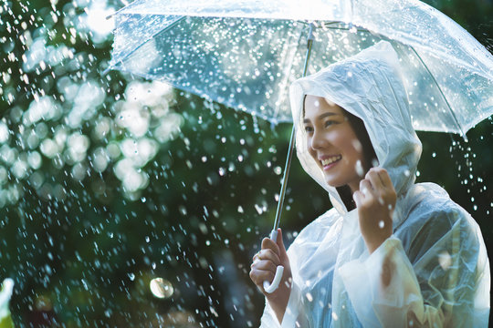 Rainy day asian woman wearing a raincoat outdoors. She is happy.