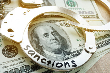 Word sanctions on a handcuffs and American dollar bills. Economical restrictive measures.