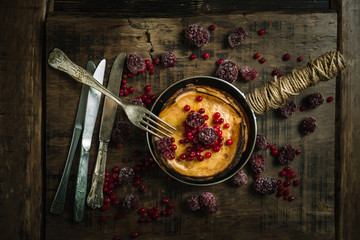 Stack of pancakes with berries on a frying pan on wood background.Top view.