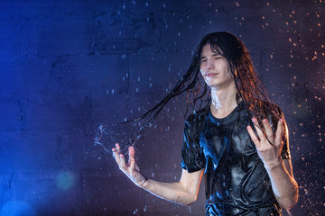 Attractive young man in black wet clothes under the rain and splash of water, studio photo