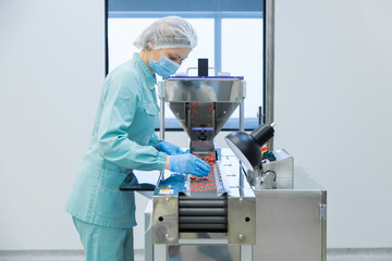 Pharmacy industry woman worker in protective clothing operating production of tablets in sterile working conditions