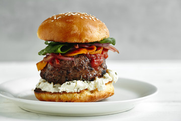 Burgers with grilled beef patties, cream cheese and spinach on classical bun. White wooden background
